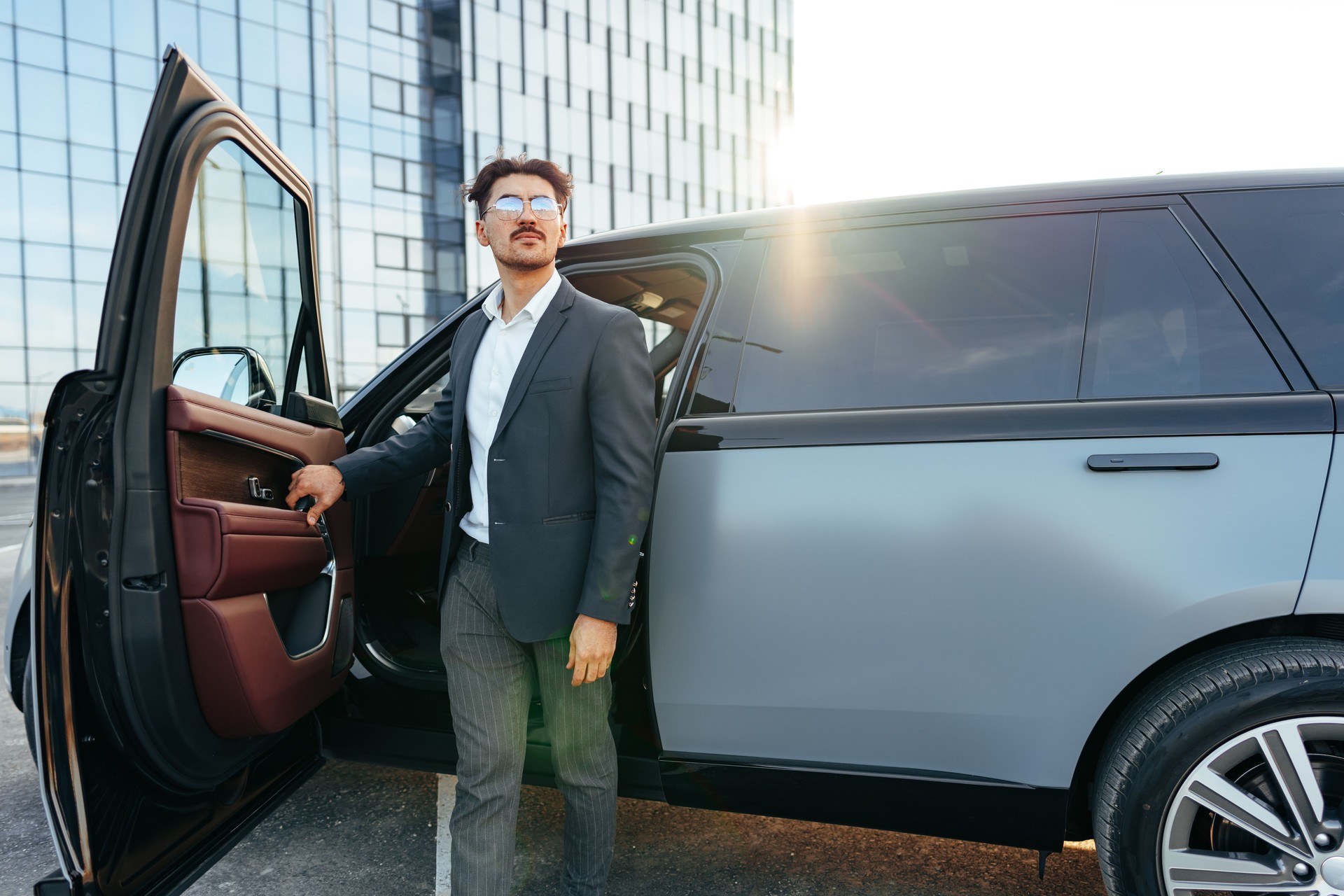 Young handsome businessman in a suit comes out of the luxury car