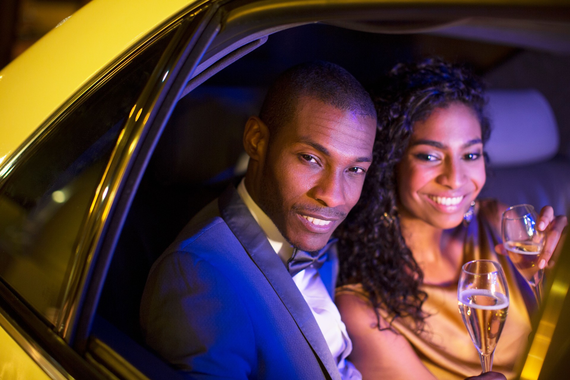 Well-dressed couple drinking champagne inside limousine