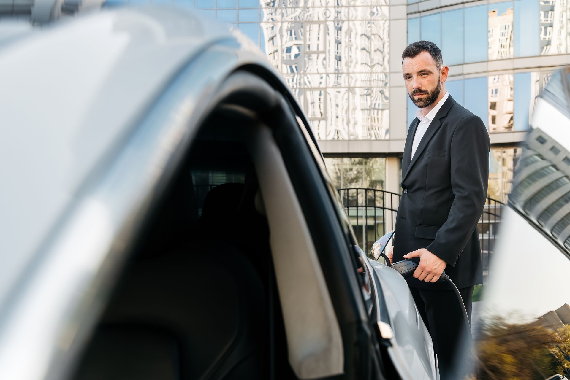 Businessman, holding power supply and charging his electric car. Clean energy and sustainability, emphasizing the importance of green technology.